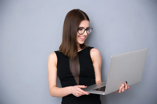 Mujer sonriente de pie con el ordenador portátil sobre fondo gris —  Fotos de Stock