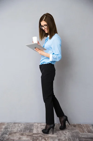 Empresária andando com xícara de café e tablet computador — Fotografia de Stock
