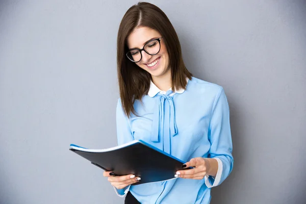 Mujer de negocios sonriente sosteniendo carpetas sobre fondo gris — Foto de Stock