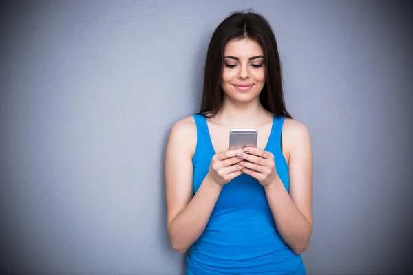 Улыбающаяся женщина с помощью смартфона на сером фоне — стоковое фото