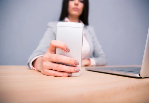 Forretningskvinde sidder ved bordet og holder smartphone - Stock-foto