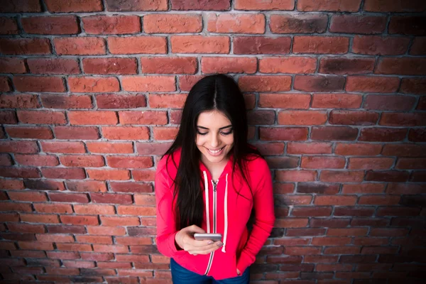 Happy woman using smartphone over brick wall — Stock Photo, Image