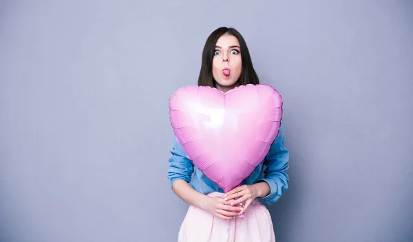 Woman holding heart shaped balloon and showing her tongue — Stock Photo, Image