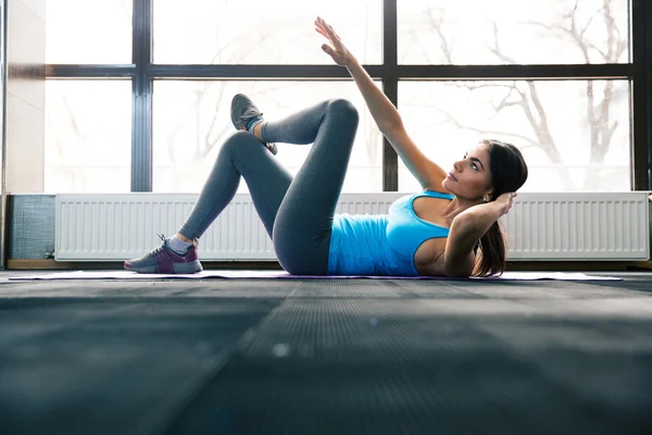 Молода жінка лежить на килимку для йоги і виконує вправи — стокове фото