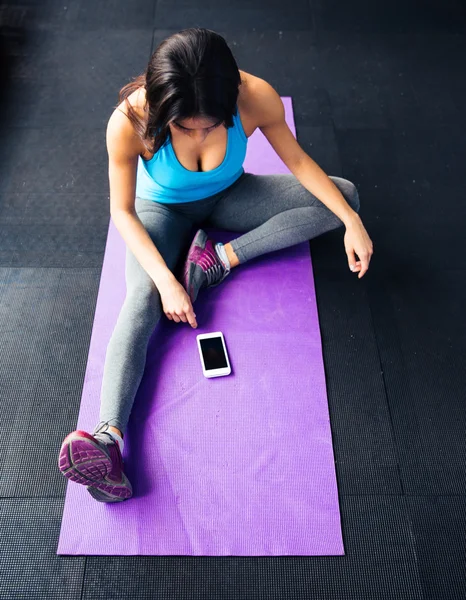 Donna seduta sul tappetino yoga e guardando sullo smartphone — Foto Stock