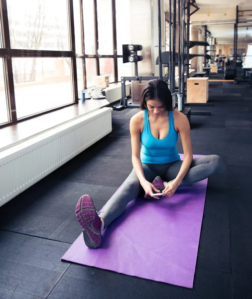 Jonge vrouw zit op de mat van de yoga en het gebruik van smartphone — Stockfoto