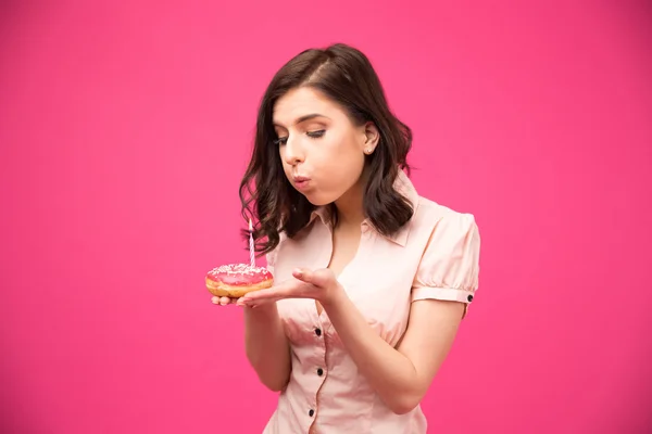 Woman holding donut and blowing on candle — Stock Photo, Image