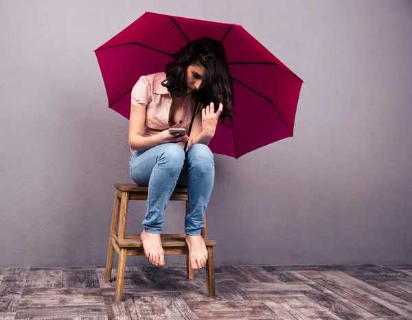 Mujer sentada en la silla con smartphone y paraguas —  Fotos de Stock