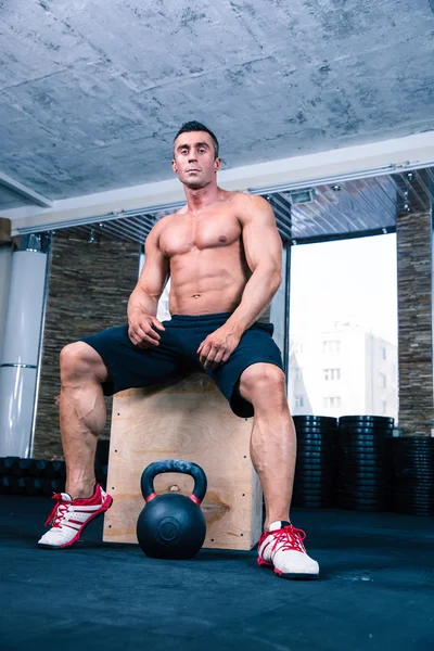 Muscular man sitting on fit box in gym