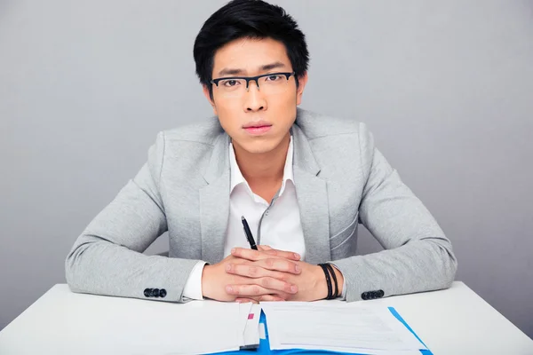 Guapo asiático hombre de negocios en gafas sentado a la mesa —  Fotos de Stock