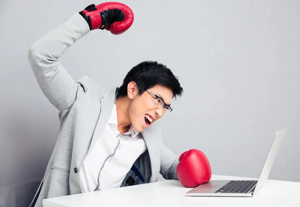 Angry businessman sitting at the table in boxing gloves — Stock Photo, Image