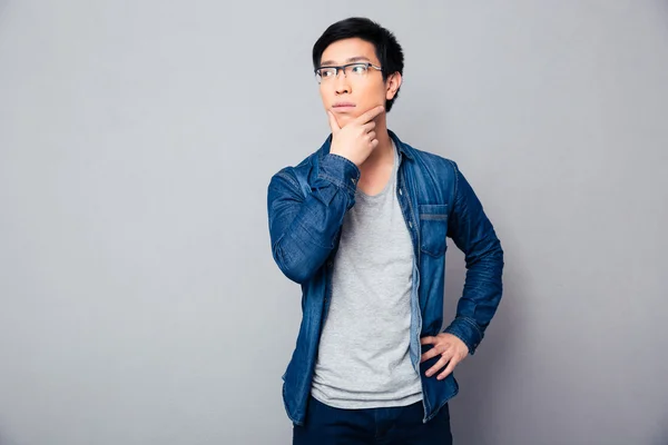 Nachdenklicher asiatischer Mann vor grauem Hintergrund — Stockfoto
