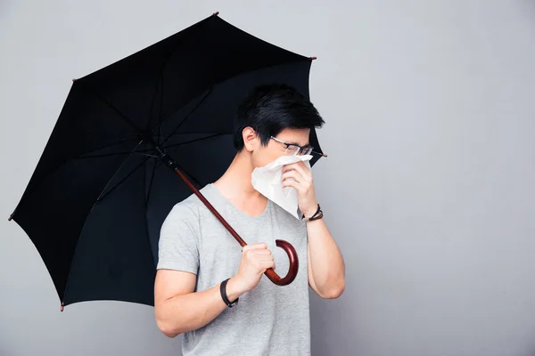 Sick asian man holding umbrella and blowing nose — Stock Photo, Image