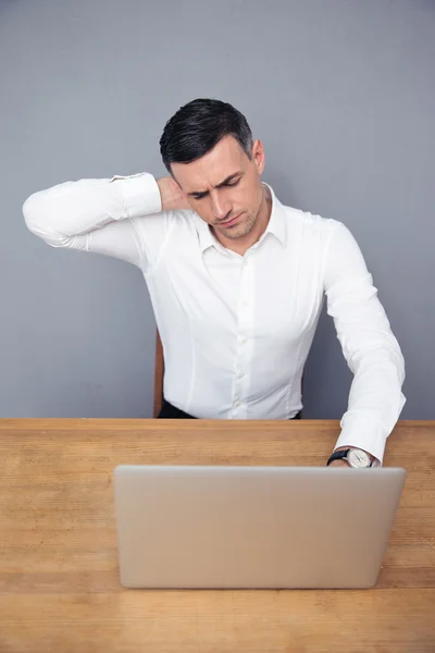 Empresário cansado sentado à mesa com laptop — Fotografia de Stock