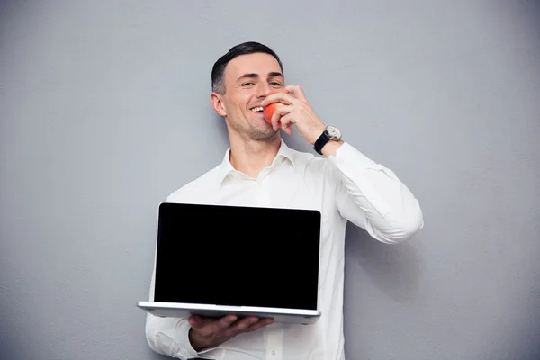 Businessman showing blank laptop screen and eating apple — Stock Photo, Image