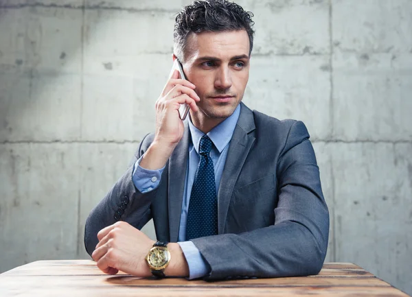 Бизнесмен, сидящий за столом и разговаривающий по телефону — стоковое фото