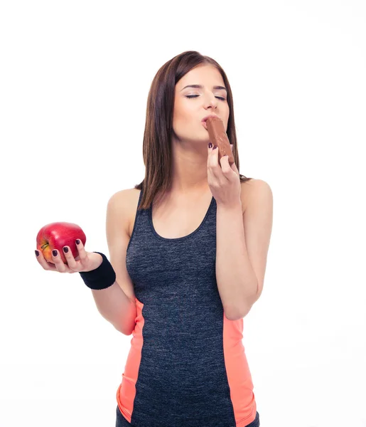 Pretty sports woman holding apple and eating chocolate — Stock Photo, Image