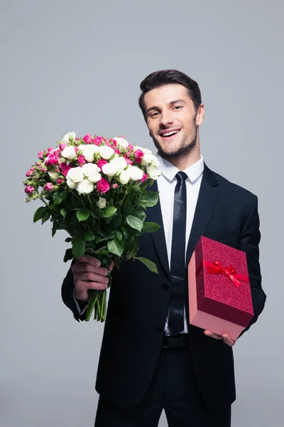 Empresário sorridente segurando flores e caixa de presente — Fotografia de Stock