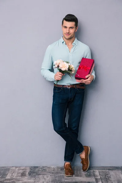 Joyeux jeune homme tenant boîte cadeau et fleurs — Photo