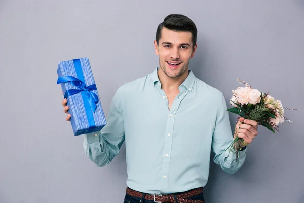 Hediye kutusu ve çiçek tutan genç casual adam — Stok fotoğraf
