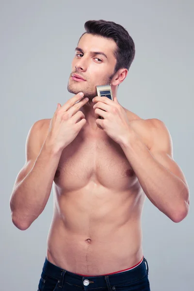 Muscular man shaving with electric razor — Stock Photo, Image