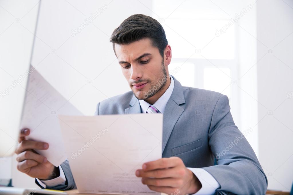 Confident businessman reading documents in office Stock Photo by  ©Vadymvdrobot 75768499