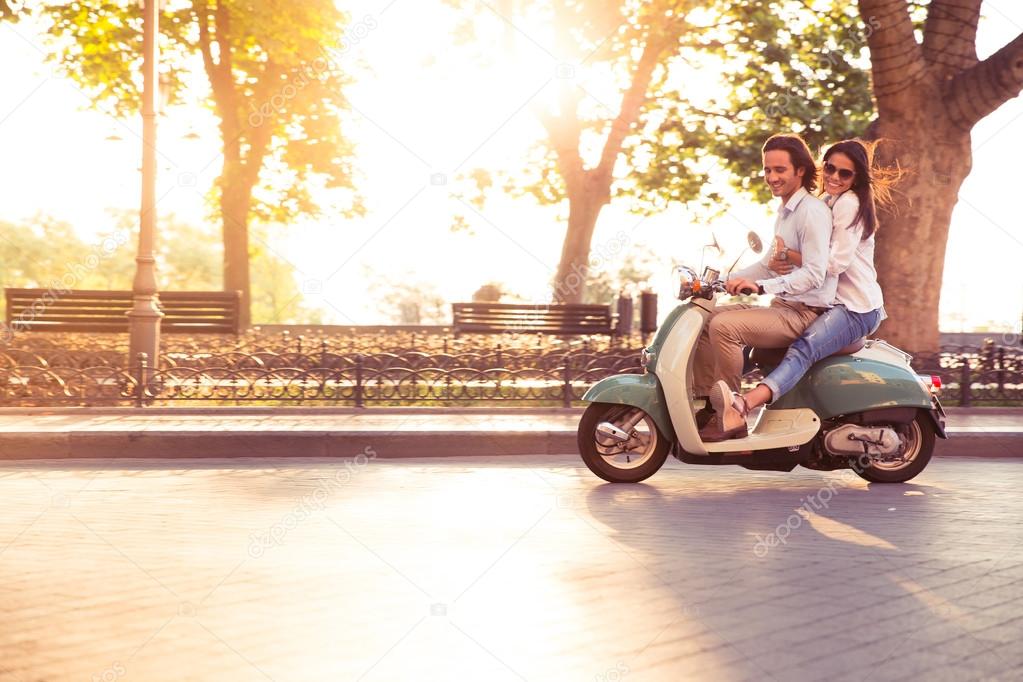 Cheerful young couple riding a scooter and having fun