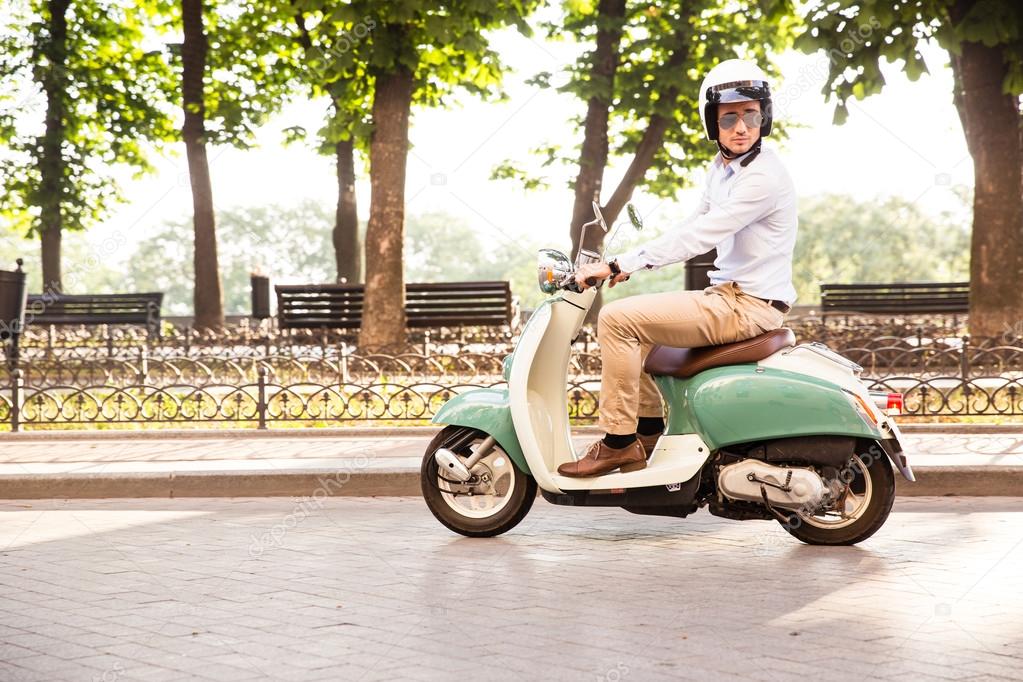 Trendy man driving a scooter in helmet