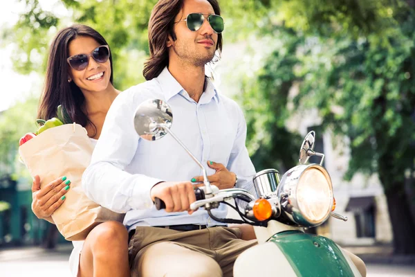 Couple driving scooter while woman holding bag full of groceries — ストック写真