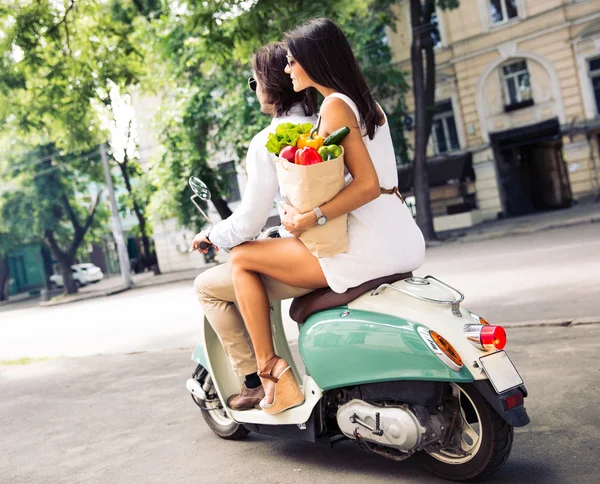 Пара на скутере, пока женщина держит сумку с покупками — стоковое фото