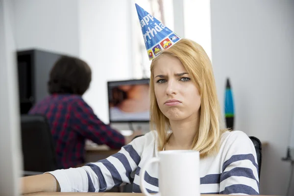 Sad woman with birthday hat sitting at the table — Stok fotoğraf