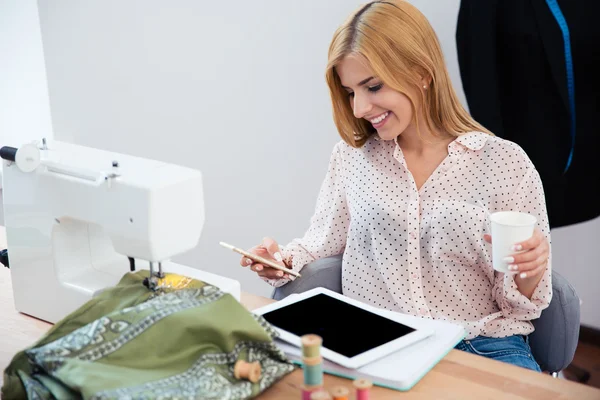 Designer segurando xícara com café e usando smartphone — Fotografia de Stock