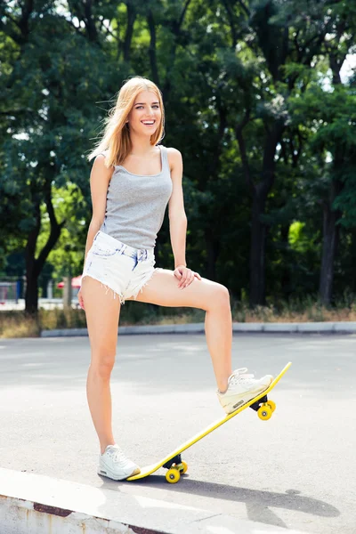 Wanita muda ceria berdiri dengan skateboard — Stok Foto