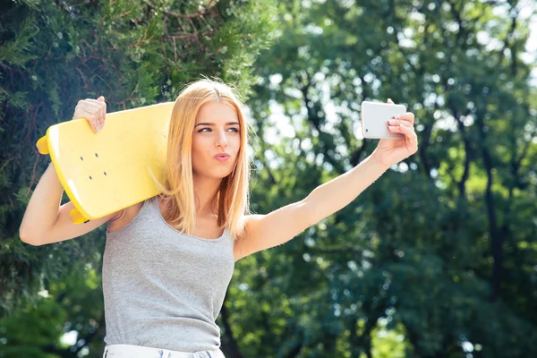 Girl with skateboard making selfie photo on smartphone — Stockfoto