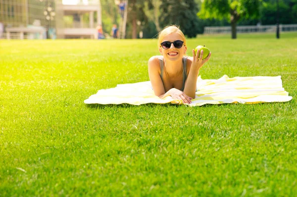 Girl lying in campus park with apple — Stock fotografie