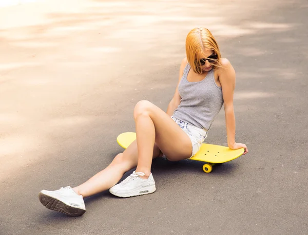 Girl in sunglasses sitting on skateboard outdoors — Stock Photo, Image