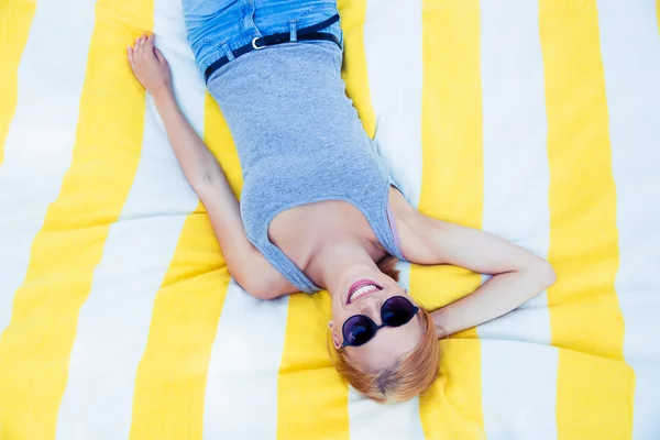 Glückliches junges Mädchen mit Sonnenbrille auf Matte liegend — Stockfoto