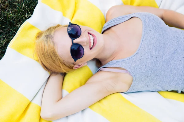 Uśmiechnięta młoda dziewczyna na okulary przeciwsłoneczne leżące na mat — Zdjęcie stockowe
