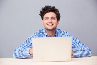 Masada dizüstü bilgisayarlı bir adam oturuyor.