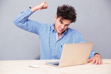 Masada dizüstü bilgisayarlı bir adam oturuyor. 