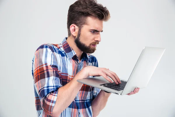 Ernsthafter junger Mann steht und benutzt Laptop — Stockfoto