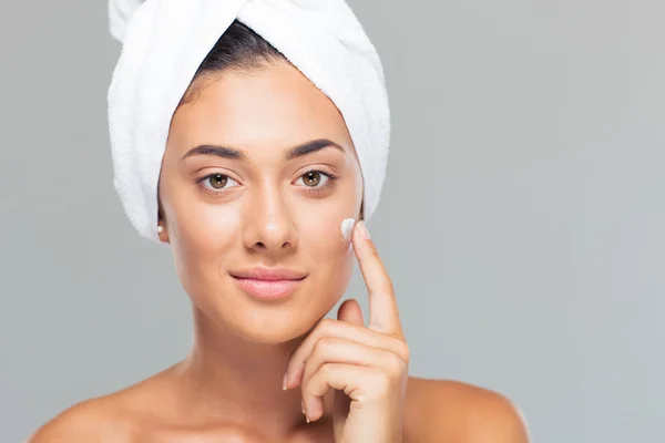 Mujer con toalla en la cabeza aplicando crema en la cara — Foto de Stock