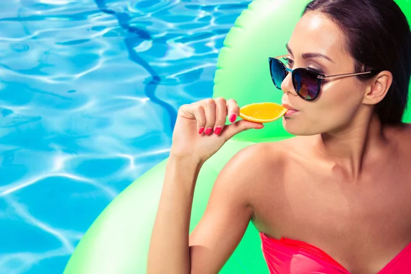 Woman eating orange in swimming pool — Stock Photo, Image