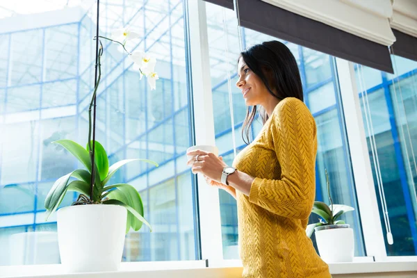 Podnikatelka, držící šálek s kávou a při pohledu na okna — Stock fotografie