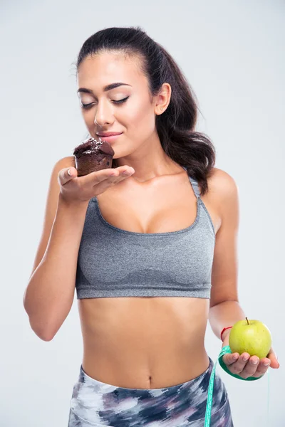 Fitness girl choosing between apple and cak — Stock Photo, Image