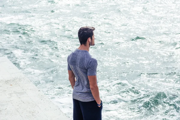 Homem em roupas esportivas de pé perto do mar — Fotografia de Stock