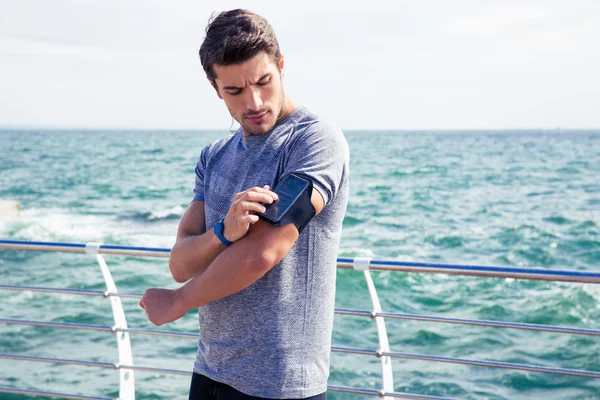 Male runner listening to music adjusting settings on armband for smartphone — Stock Photo, Image