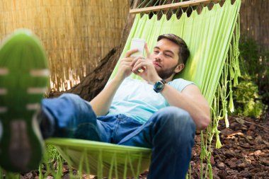 Hammok üzerinde akıllı telefon kullanan adam 