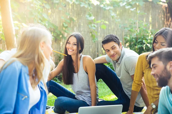 Happy friends sitting with laptop outdoors — Stock Photo, Image