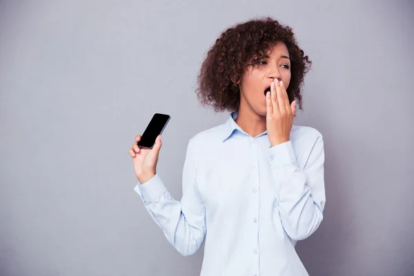 Afro american woman yawning while holding smartphone — Stock Photo, Image
